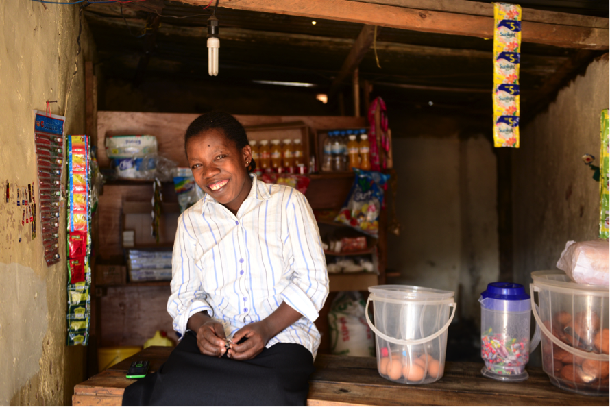 Vestine Twizere smiles proudly at her kiosk selling candies, vegetables, and drinks