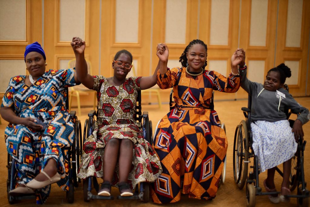 Four African woman, all wheelchair users, hold hands in unity. 