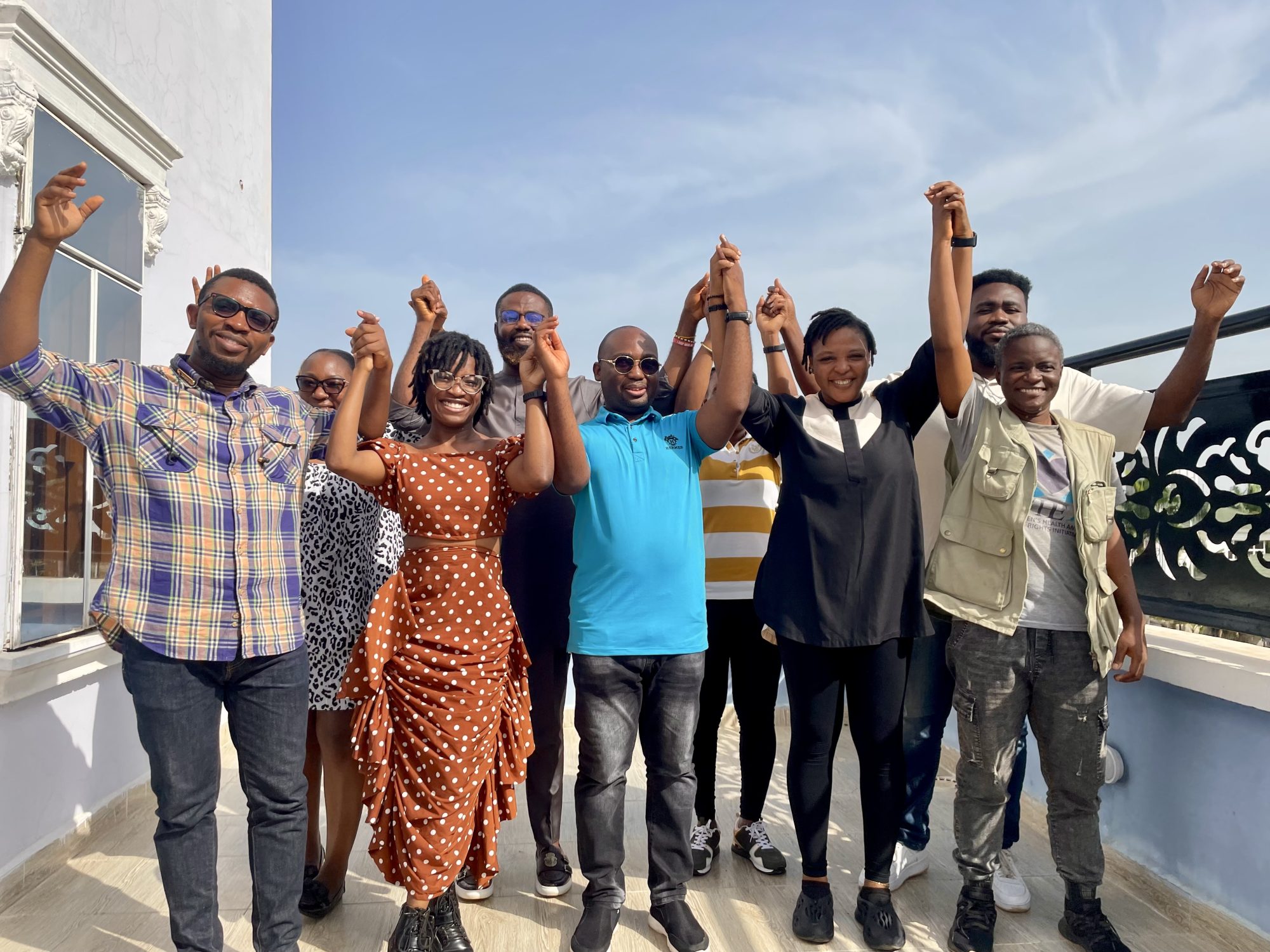 A group of Nigerian activists (men and women) are holding hands in unity and smiling outside.