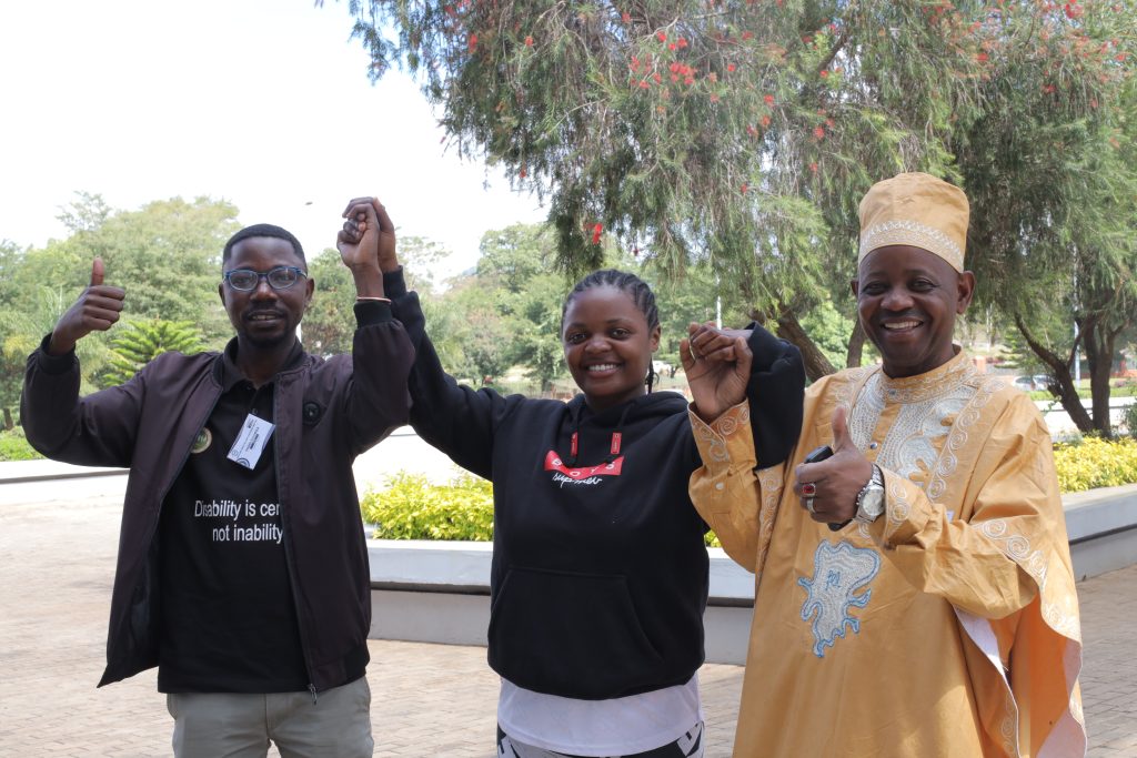 Three people, two men and a woman, join hands and are smiling.