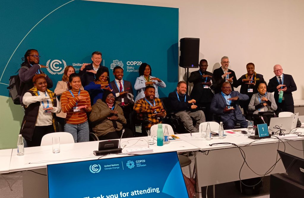 Members of the Disability Climate Caucus, posing for a group photo against the background of COP banner.