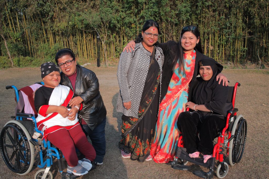 Five women with disabilities from Nepal are smiling and wrapping their arms around each other outside. 