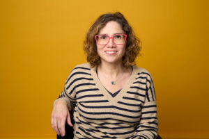 Portrait shot of Cata wearing red glasses and a striped brown and black top