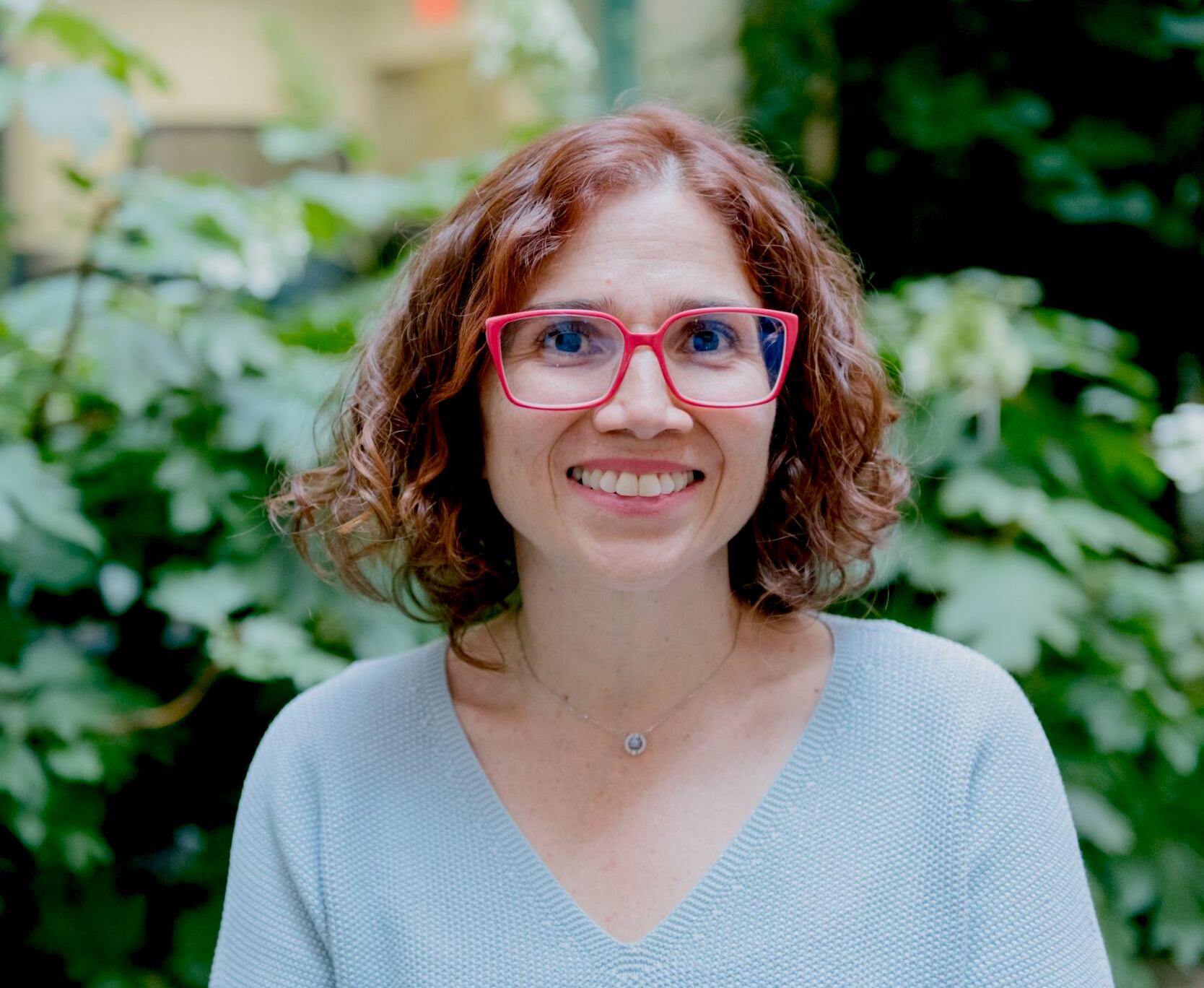 A portrait image of Catalina who is wearing red glasses and smiling.