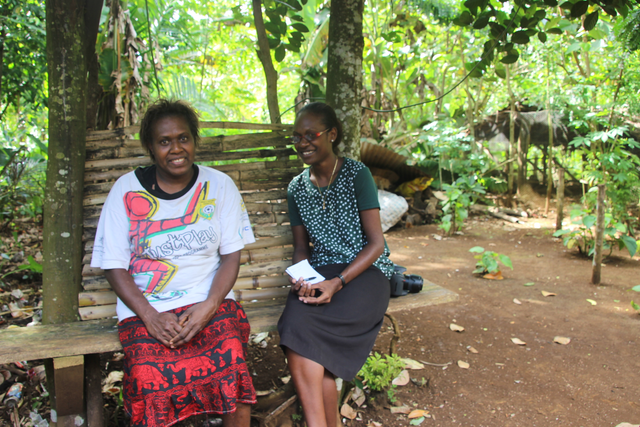 Two ladies sitting on a bench smiling. 