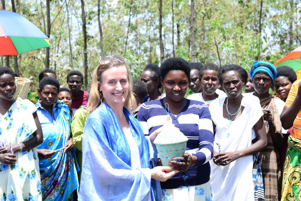 Diana, a white woman with blonde hair, wearing glasses on her head and a blue dress stands with women grantees