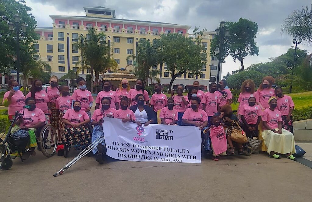 Women with disabilities pose for a group photo wearing pink t-shirts. In the front is a DRF banner.