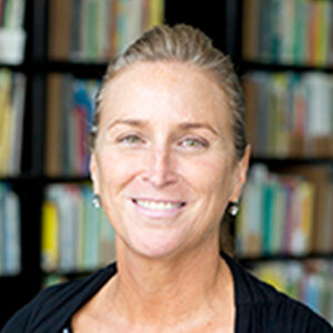 Photo of Maureen smiling and standing in front of a bookshelf. 