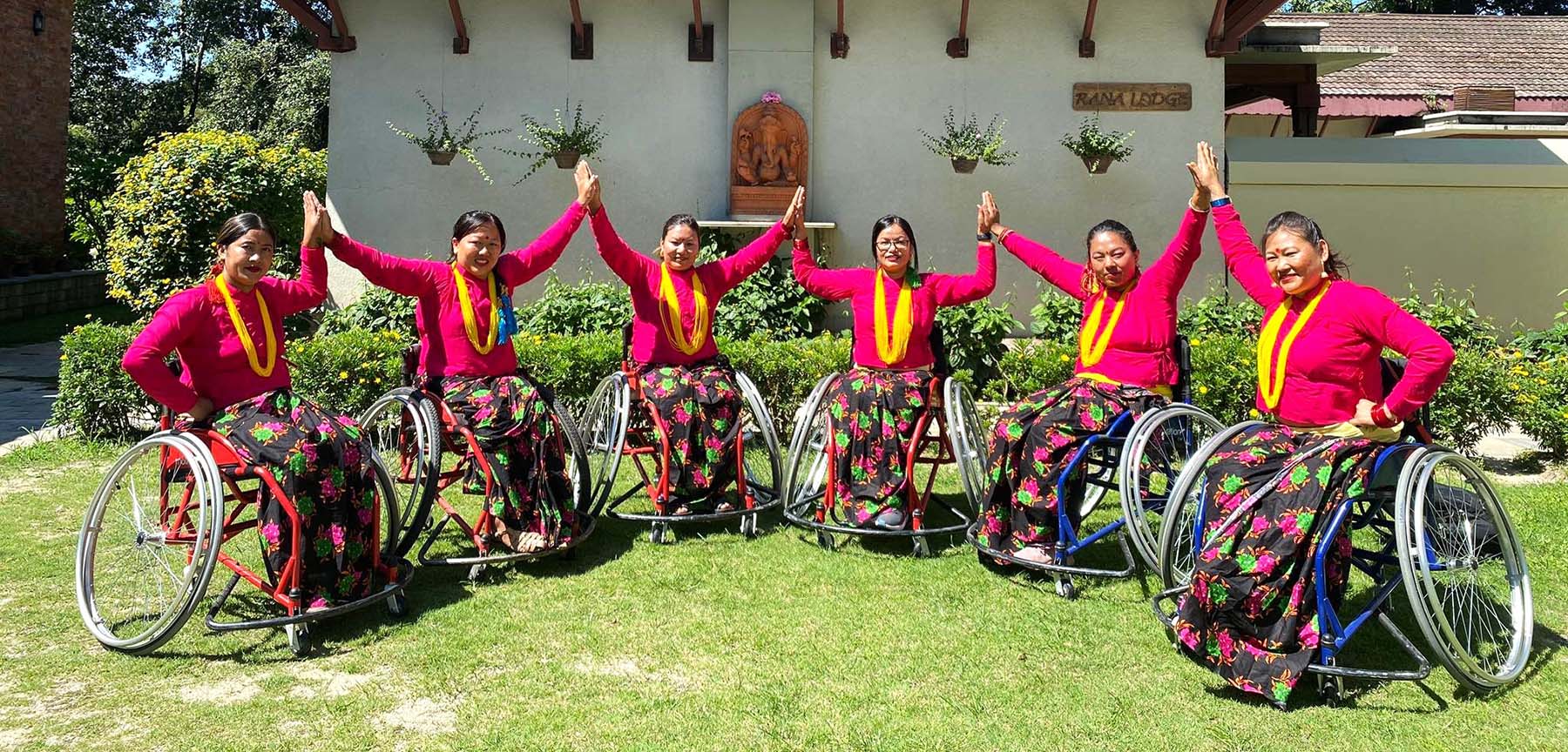Women using wheelchairs and wearing yellow garlands join hands in Nepal.