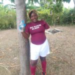 Nancy, a Haitian woman wearing a soccer uniform smiles at the camera.
