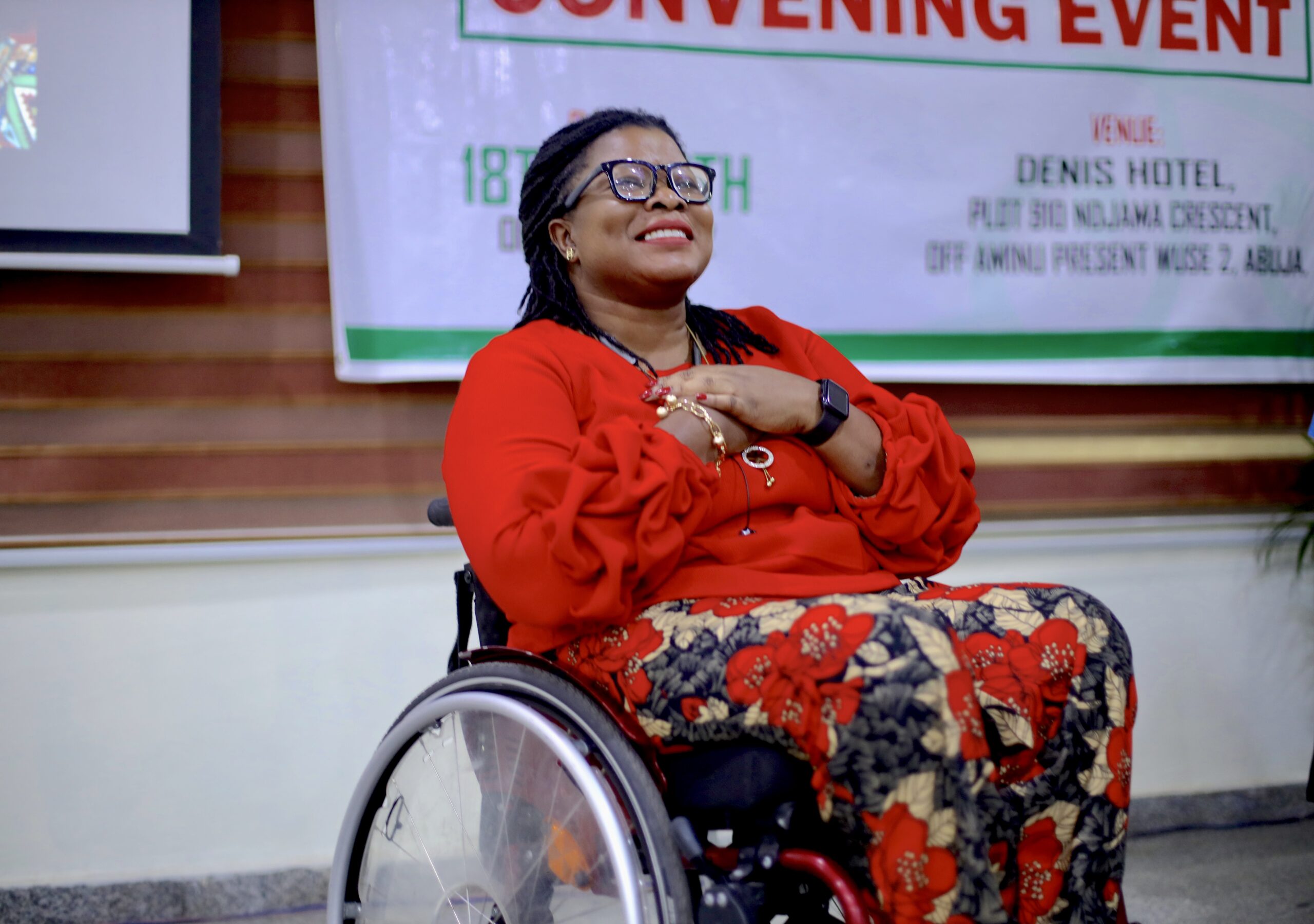 Grace Jerry sits on a wheelchair and smiles with her hands on her heart.